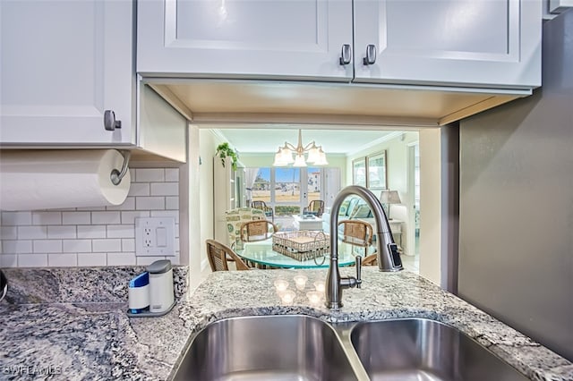 kitchen featuring sink, white cabinetry, ornamental molding, light stone countertops, and decorative backsplash