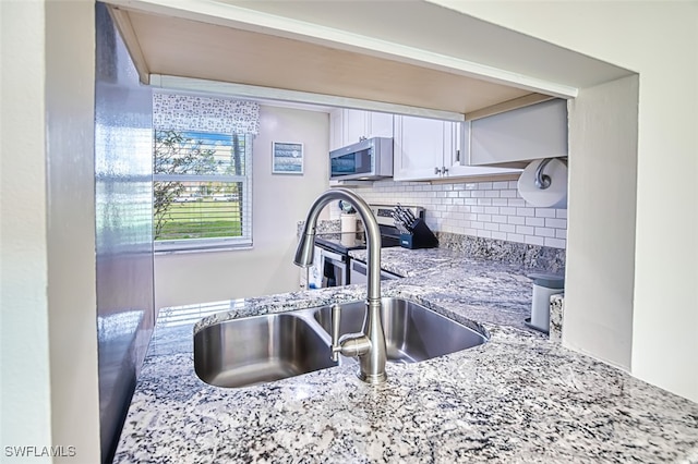 kitchen with light stone counters, sink, decorative backsplash, and white cabinets