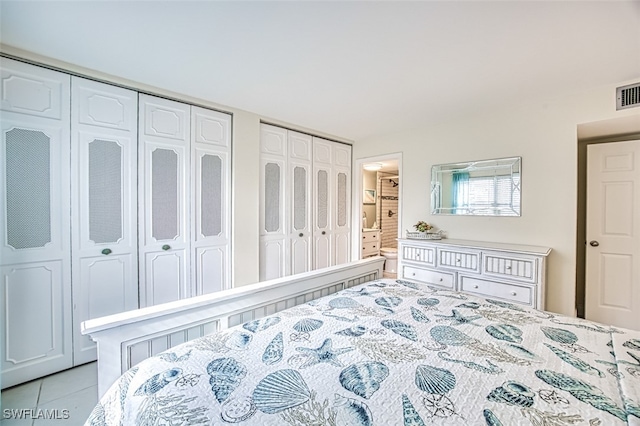 bedroom featuring multiple closets, ensuite bath, and light tile patterned flooring