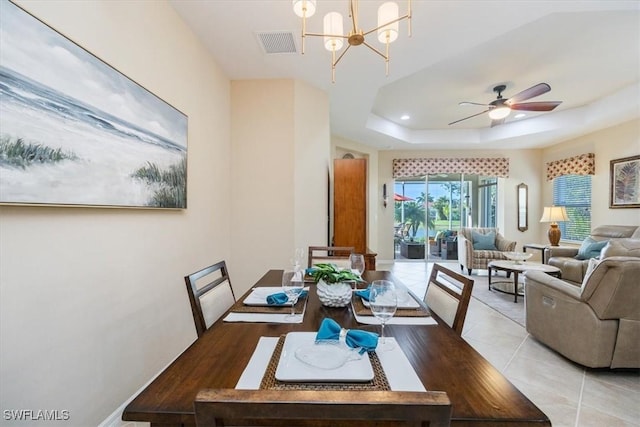 tiled dining area featuring ceiling fan with notable chandelier and a tray ceiling