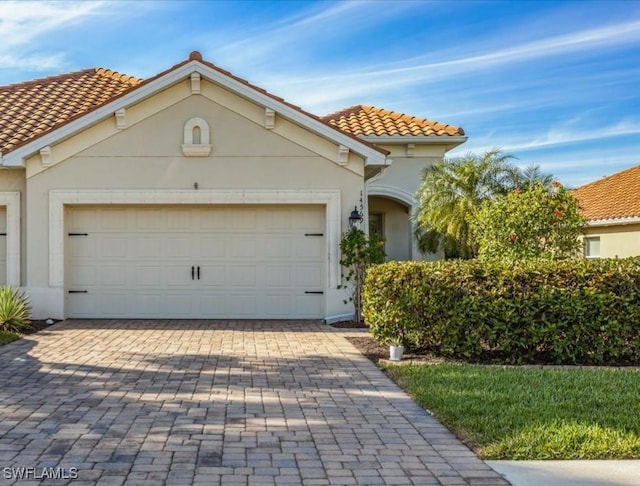 mediterranean / spanish house with a garage, a tiled roof, decorative driveway, and stucco siding