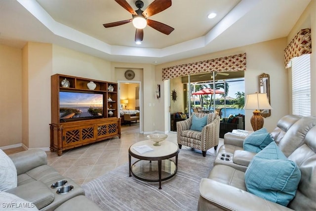 tiled living room with ceiling fan and a tray ceiling