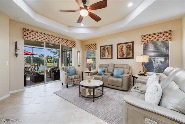 living room featuring ceiling fan, a raised ceiling, and light tile patterned floors