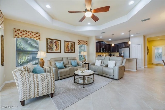 living room featuring a tray ceiling, light tile patterned floors, and a wealth of natural light