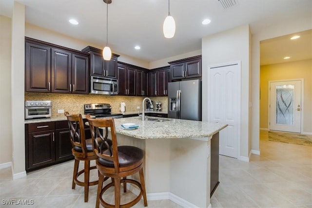 kitchen featuring light stone counters, dark brown cabinets, stainless steel appliances, and a center island with sink