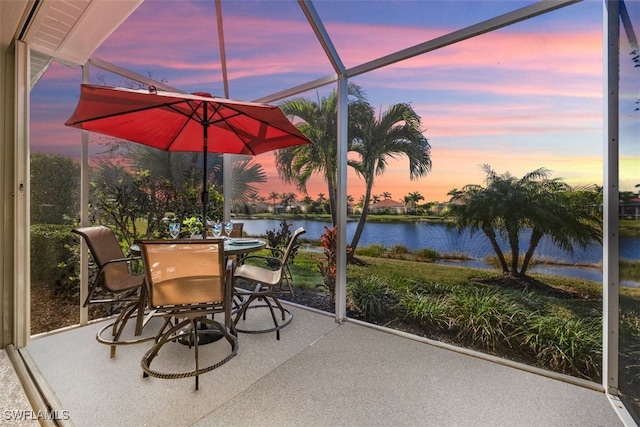 patio terrace at dusk featuring a lanai, a water view, and outdoor dining space