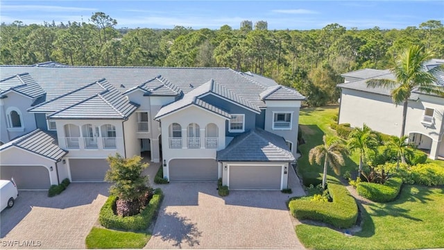 view of front of house featuring a wooded view, a tiled roof, decorative driveway, a garage, and stucco siding