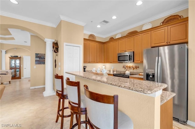 kitchen with decorative columns, a kitchen island, appliances with stainless steel finishes, and light stone counters