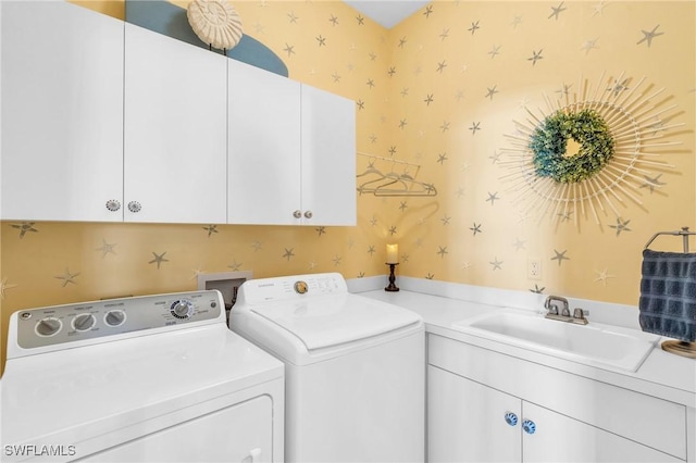 clothes washing area featuring a sink, cabinet space, wallpapered walls, and washer and clothes dryer