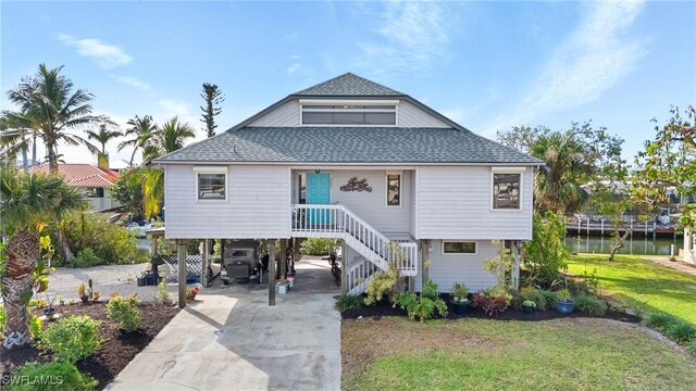 raised beach house with a carport, a water view, and a front yard