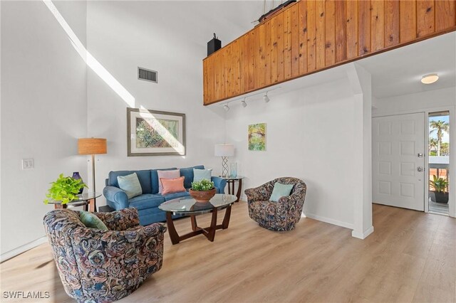 living room featuring a towering ceiling, rail lighting, and light hardwood / wood-style flooring