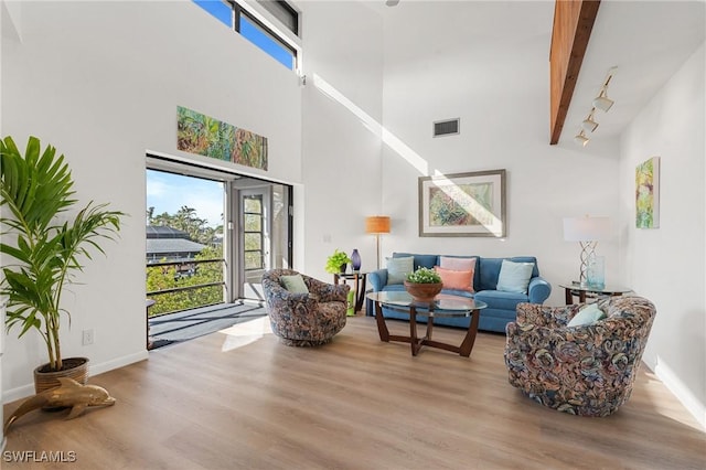 living room with beamed ceiling, a towering ceiling, and light hardwood / wood-style flooring