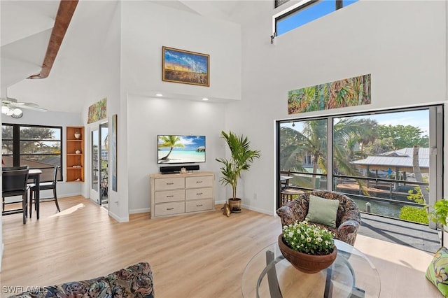 living room featuring a towering ceiling, ceiling fan, and light wood-type flooring