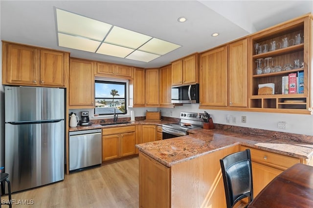 kitchen with sink, light wood-type flooring, kitchen peninsula, stainless steel appliances, and light stone countertops