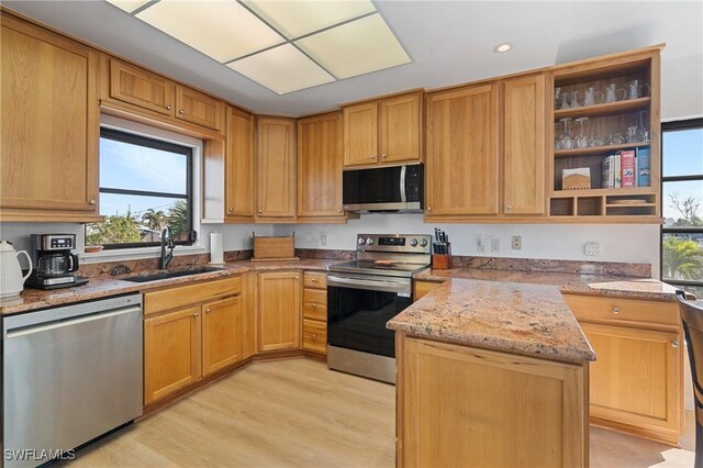 kitchen featuring appliances with stainless steel finishes, sink, light stone counters, kitchen peninsula, and light hardwood / wood-style flooring