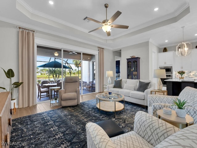 living room featuring light hardwood / wood-style floors, a raised ceiling, and ceiling fan with notable chandelier