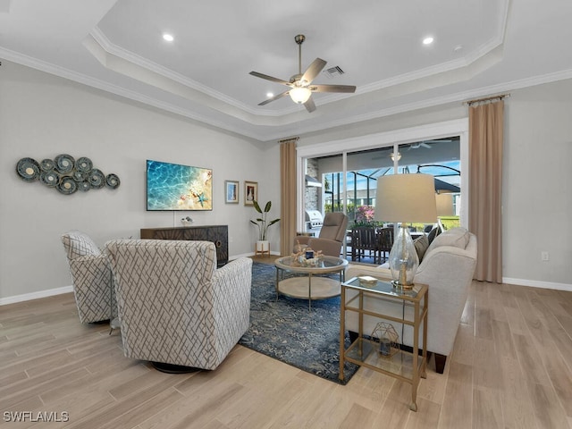 living room with crown molding, a tray ceiling, light hardwood / wood-style floors, and ceiling fan