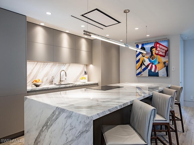 kitchen featuring a spacious island, sink, black electric cooktop, and decorative light fixtures