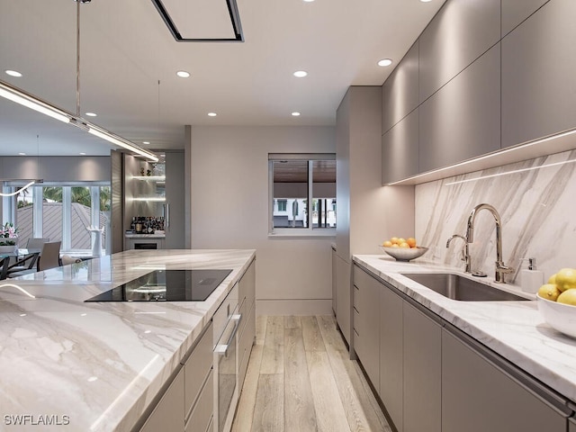 kitchen featuring black electric cooktop, sink, light stone counters, and gray cabinets