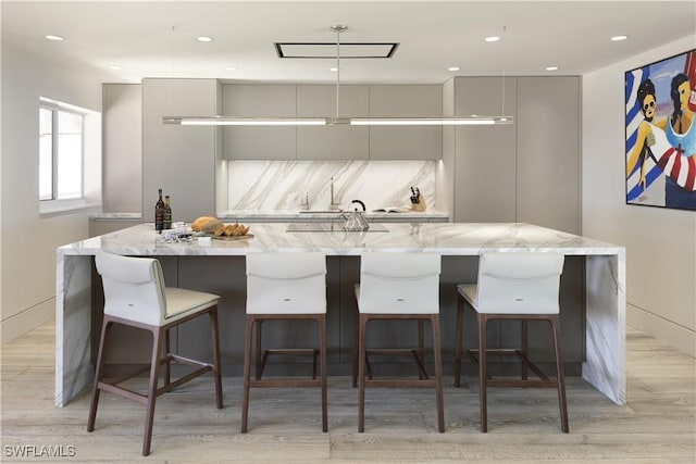 kitchen featuring a large island, a kitchen breakfast bar, light stone countertops, and decorative backsplash