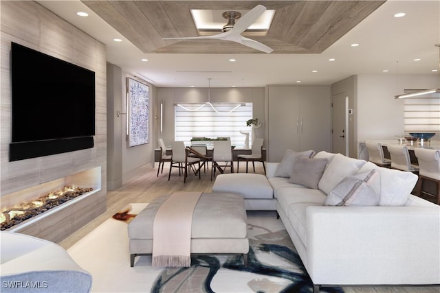 living room with a tray ceiling, light hardwood / wood-style floors, ceiling fan, and a multi sided fireplace