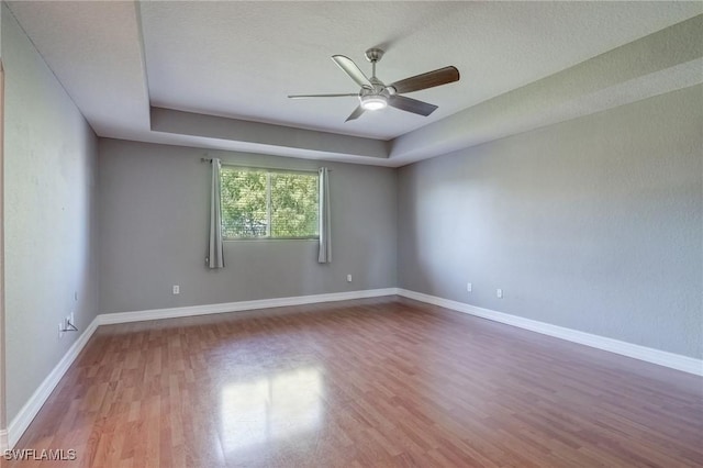 unfurnished room featuring a raised ceiling, hardwood / wood-style floors, a textured ceiling, and ceiling fan