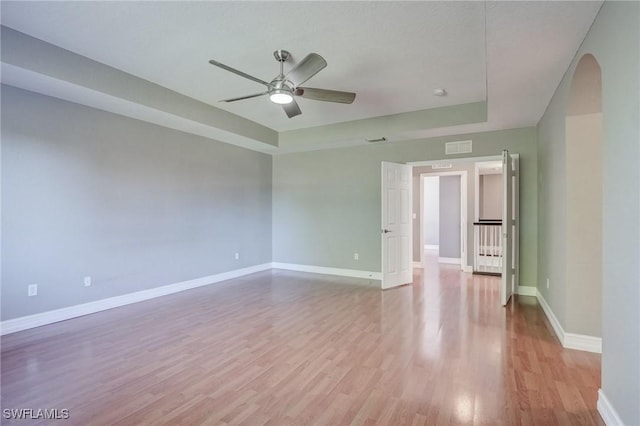 spare room featuring a raised ceiling, ceiling fan, and light hardwood / wood-style floors