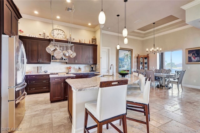 kitchen featuring an island with sink, sink, stainless steel fridge, a kitchen breakfast bar, and hanging light fixtures