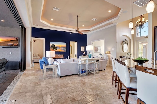 living room with ornamental molding, a tray ceiling, ceiling fan with notable chandelier, and a high ceiling