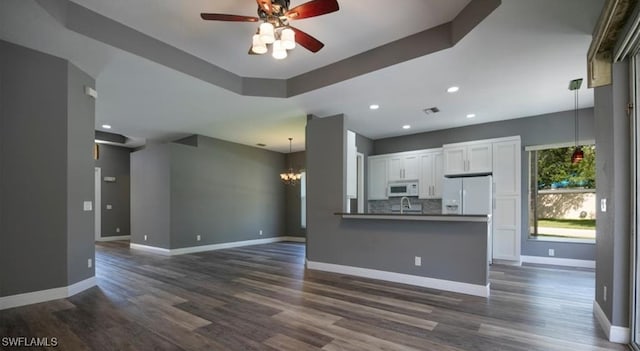 unfurnished living room with a tray ceiling, dark wood-type flooring, and ceiling fan with notable chandelier