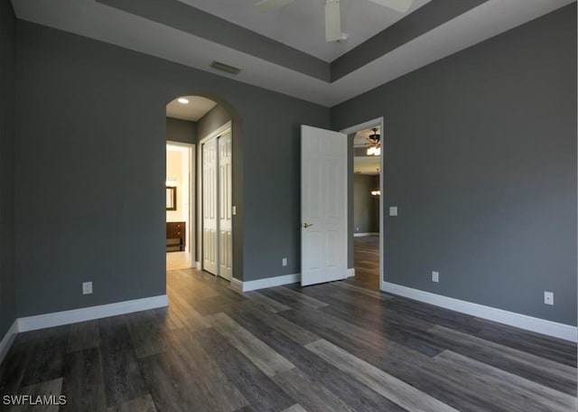 unfurnished room with ceiling fan, dark hardwood / wood-style flooring, and a raised ceiling