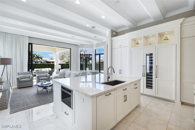 kitchen with sink, white cabinetry, stainless steel microwave, light stone countertops, and a kitchen island with sink