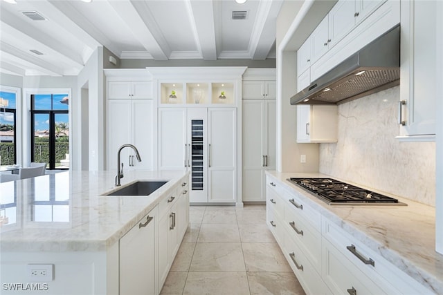 kitchen featuring sink, white cabinetry, stainless steel gas stovetop, light stone countertops, and a kitchen island with sink