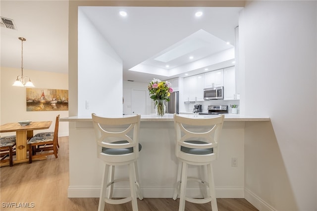 kitchen featuring a breakfast bar, decorative light fixtures, white cabinets, kitchen peninsula, and stainless steel appliances