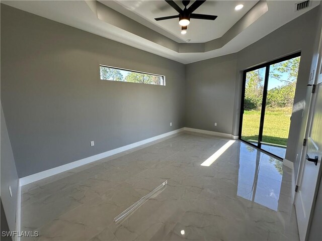 unfurnished room with a raised ceiling, a healthy amount of sunlight, and ceiling fan