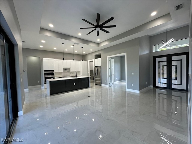 kitchen featuring stainless steel appliances, a kitchen island with sink, white cabinets, and a tray ceiling