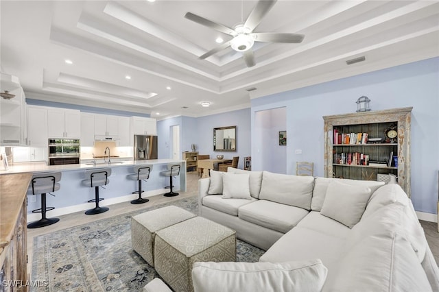 living room with sink, a tray ceiling, and ceiling fan