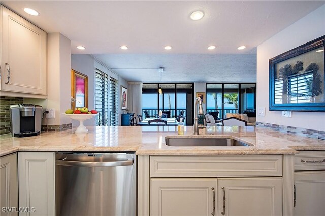 kitchen with decorative light fixtures, dishwasher, sink, light stone counters, and kitchen peninsula