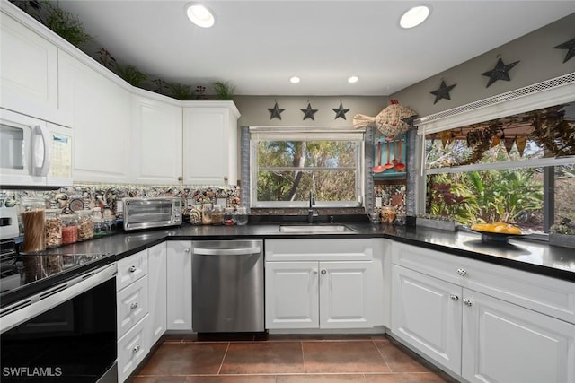 kitchen with stainless steel appliances, dark tile patterned floors, sink, and white cabinets