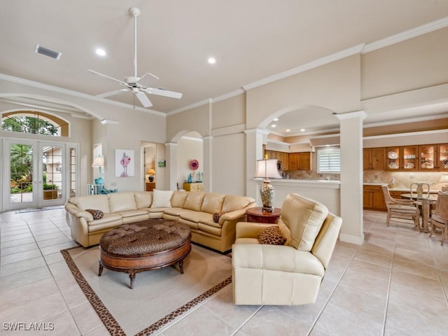 tiled living room with crown molding, ceiling fan, decorative columns, a high ceiling, and french doors