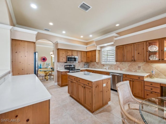 kitchen featuring light tile patterned flooring, ornamental molding, a kitchen island, stainless steel appliances, and decorative backsplash