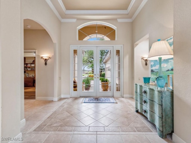 tiled foyer with french doors, a towering ceiling, ornamental molding, and a raised ceiling