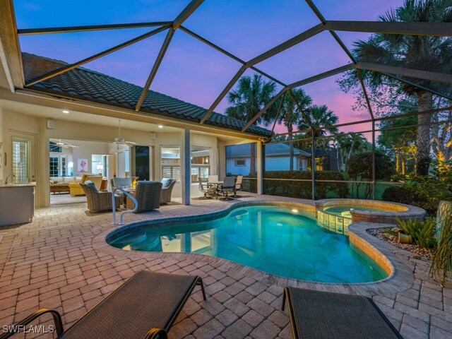 pool at dusk featuring ceiling fan, a patio, glass enclosure, an outdoor hangout area, and an in ground hot tub