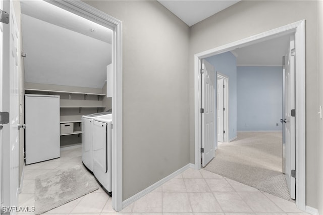 corridor featuring baseboards, light tile patterned flooring, light colored carpet, and washing machine and clothes dryer