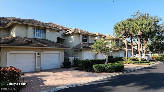 view of front facade featuring a garage, a tile roof, decorative driveway, and stucco siding