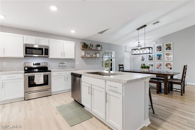 kitchen with white cabinetry, hanging light fixtures, stainless steel appliances, and a center island with sink