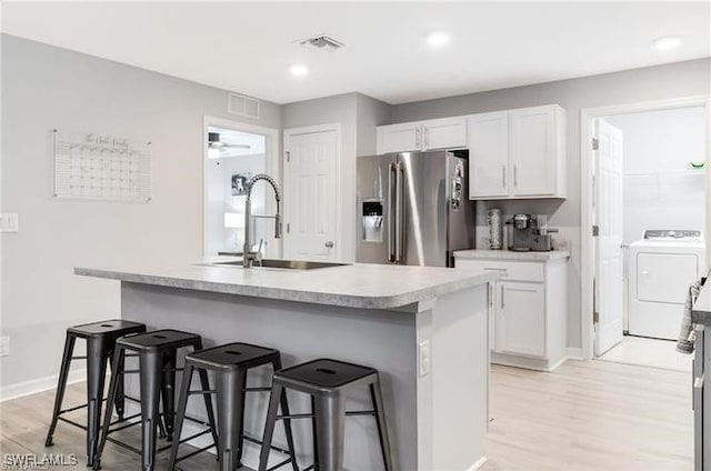 kitchen with white cabinets, washer / dryer, high end fridge, and a kitchen island with sink