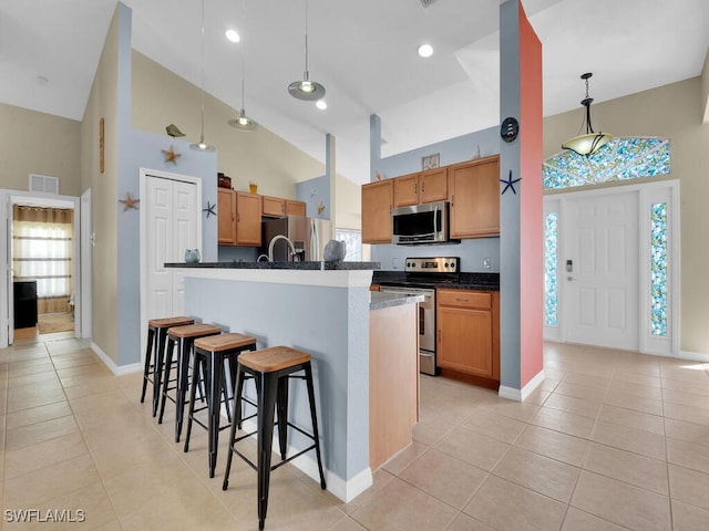 kitchen with stainless steel appliances, decorative light fixtures, a center island with sink, and light tile patterned floors