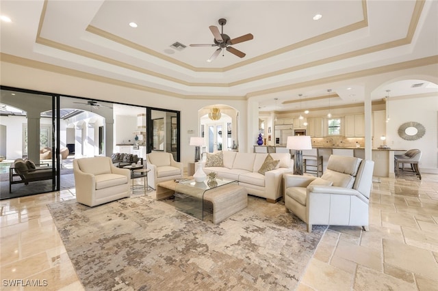 living room with crown molding, a tray ceiling, and ceiling fan