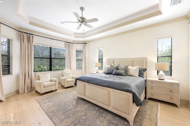 bedroom featuring multiple windows, light wood-type flooring, and a tray ceiling